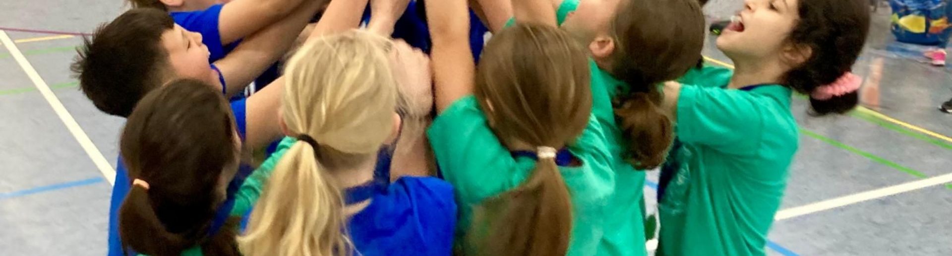 Viele Kinder stehen in einer Turnhalle im Kreis und strecken gemeinsam einen Pokal in die Höhe.
